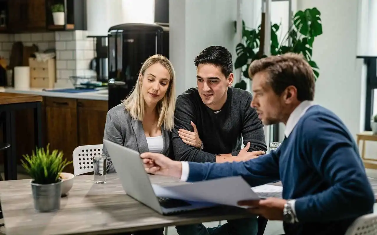 A man and woman sit at a table with a laptop, discussing strategies for building a successful financial advisory practice.
